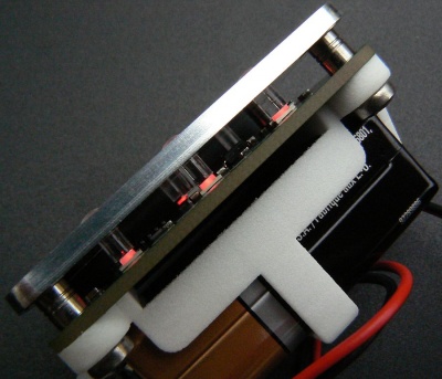 Aufbau des Endprodukts. Grün - die Leiterplatte mit LEDs und den anderen Bauteilen. Alu - die Frontplatte. Weiß - die 9V Batteriehalterung. Die Gewindebolzen sind von hinten in die Frontplatte eingepresst, so dass deren Front keine Montageelemente zeigt. Die Lichtleiter aus Plexiglas werden frontseitig durch die Aluminiumplatte eingesteckt, so dass sie exakt auf den LEDs sitzen. Alle drei Elemente werden gemeinsam "von hinten" verschraubt.